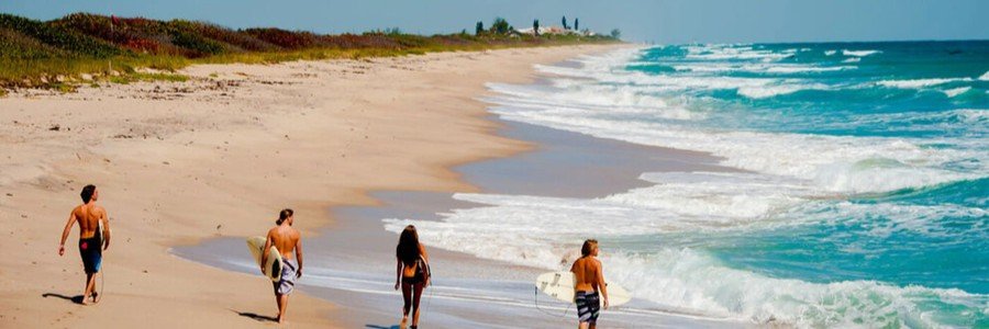Surfers walking along a sandy beach carrying surfboards beside the Atlantic Ocean