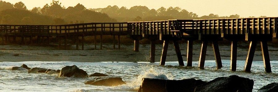 Wooden fishing pier stretching into the Atlantic Ocean along the rocky shoreline of Amelia Island, Florida during golden hour.