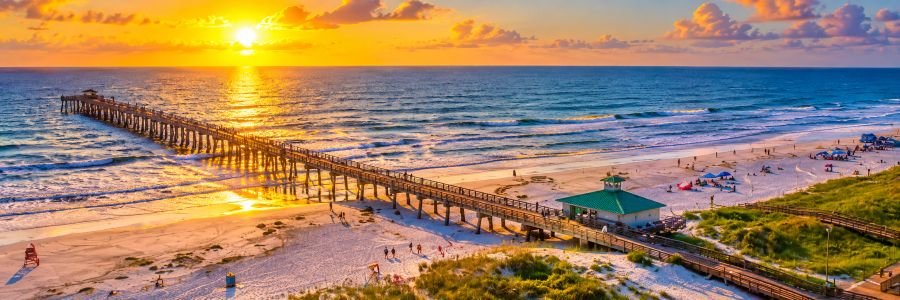 Long ocean pier stretching across a sandy Amelia Island beach during a glowing coastal sunset.