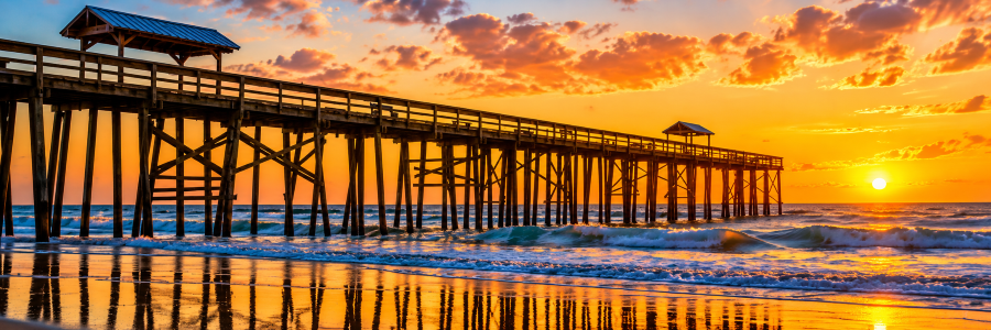 Wooden pier stretching over the Atlantic Ocean during a colorful sunset in Fernandina Beach, Florida.