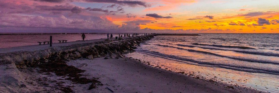 Orange and purple sunset above the rocky South Jetty and waves at Fort Pierce Inlet.