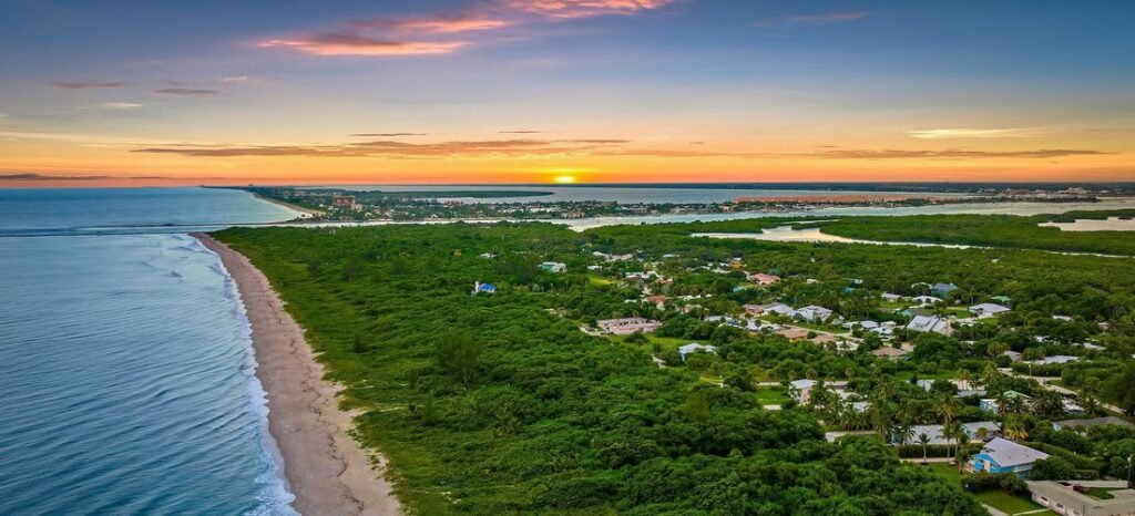 Aerial panoramic view of a lush green barrier island beach coastline and coastal neighborhood at sunset in Hobe Sound, Florida.