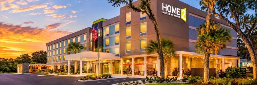 Home2 Suites by Hilton in with palm trees and welcoming outdoor spaces at sunset.