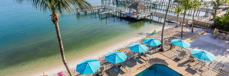 Waterfront pool, blue umbrellas, sandy lagoon beach, and dock at Hutchinson Island Hotel.