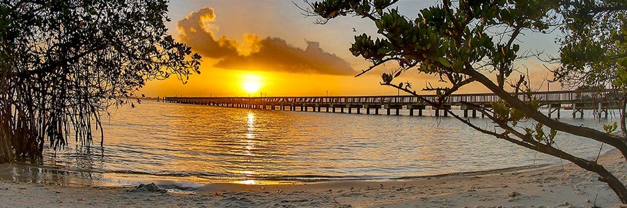 Sunrise over the Indian River Lagoon on Hutchinson Island, Florida, with a fishing pier and sandy shoreline.