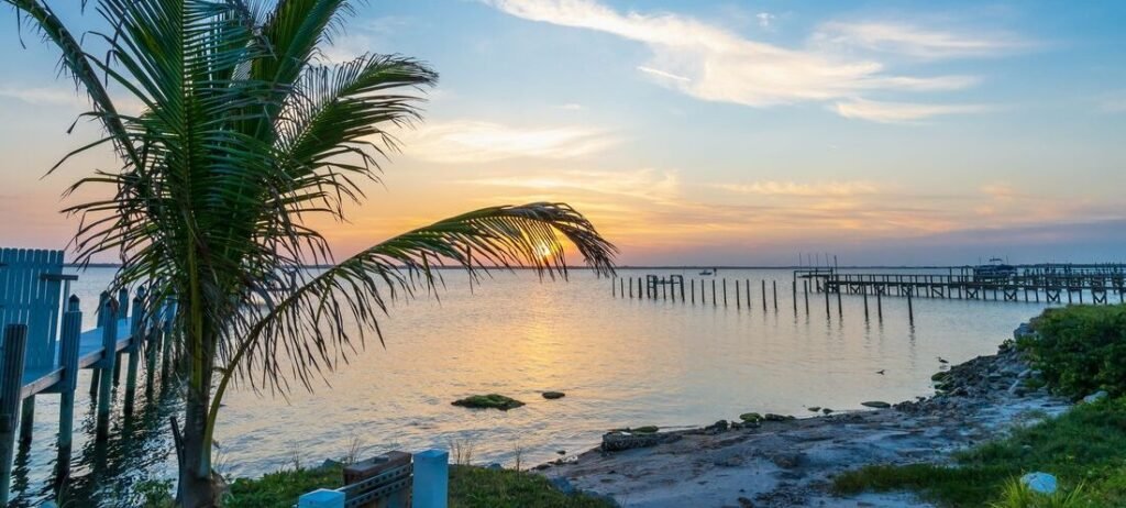 Sunset over the Indian River Lagoon framed by a palm tree and private docks in Indian River Shores, Florida.