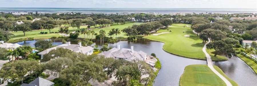Aerial view of luxury homes, winding waterways, palm trees, and a green golf course in Indian River Shores, Florida.