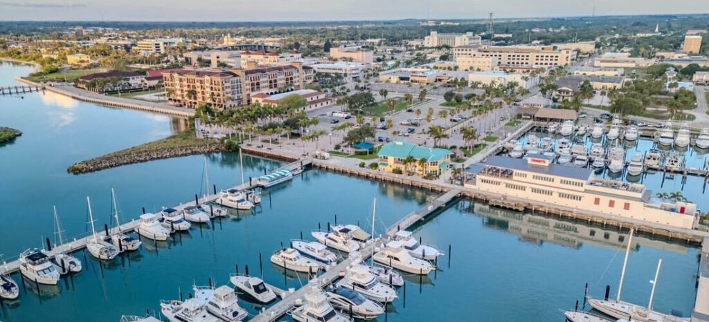 Aerial view of luxury boats docked at a calm coastal marina waterfront next to palm trees and seaside buildings, Port St Lucie