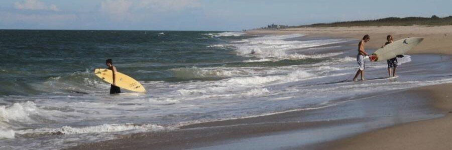Surfing Along the Sebastian Coast | Beach Travel Destinations Surfers entering Atlantic waves from a sandy beach near Sebastian, Florida