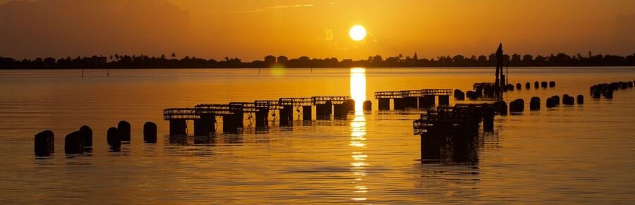 Golden Sunset Over the Indian River Lagoon | Beach Travel Destinations Golden sunset over calm water and old wooden pilings along the Sebastian waterfront