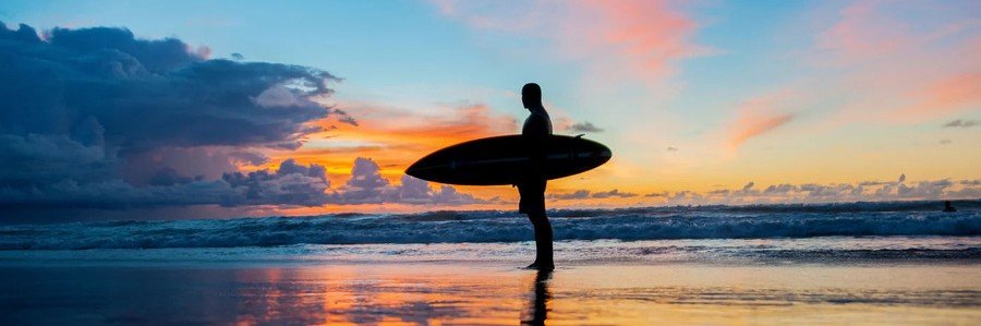 Surfer carrying a surfboard along the beach at sunset near Sebastian Inlet, Florida.