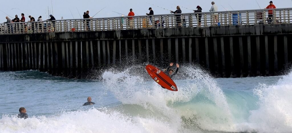 Surfer riding a wave near anglers fishing from Sebastian Inlet jetty in Florida.