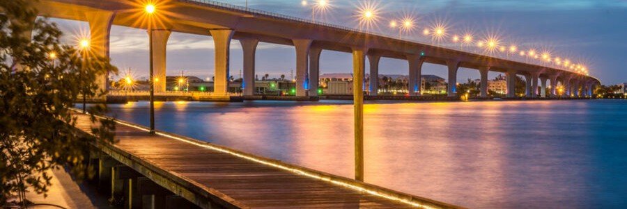 The Stuart Riverwalk and Roosevelt Bridge illuminated at dusk over the St. Lucie River in Stuart, Florida.