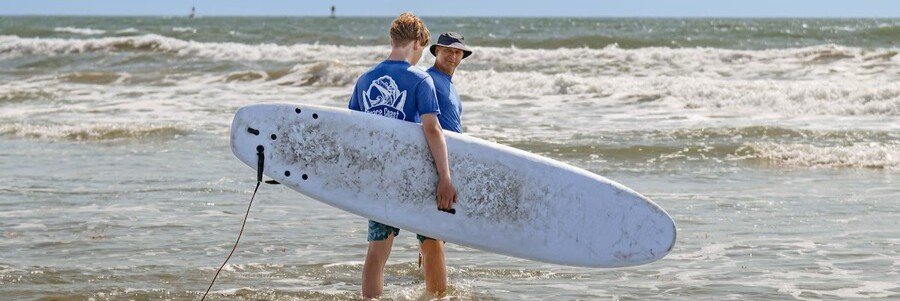 Surf instructor and student carrying a surfboard at Melbourne Beach, Florida.