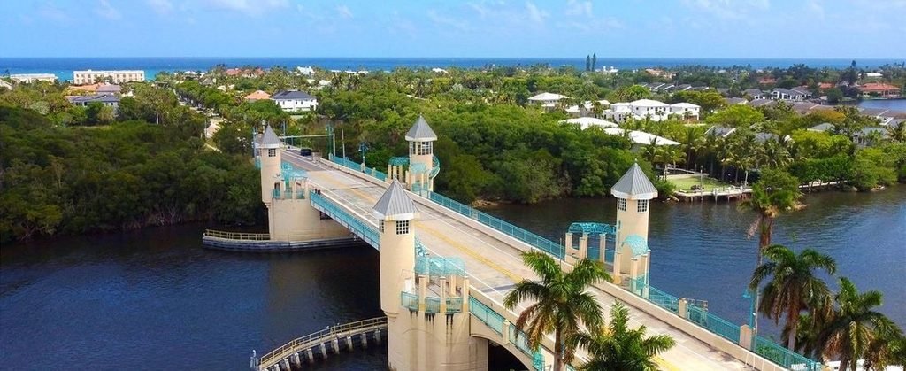Aerial view of the Ocean Avenue Bridge crossing the Intracoastal Waterway, featuring turquoise railings, decorative towers, and palm trees.