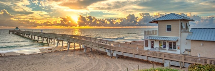 Deerfield Beach International Fishing Pier stretching over the Atlantic Ocean beneath a golden sky, with sunlight reflecting across the water.