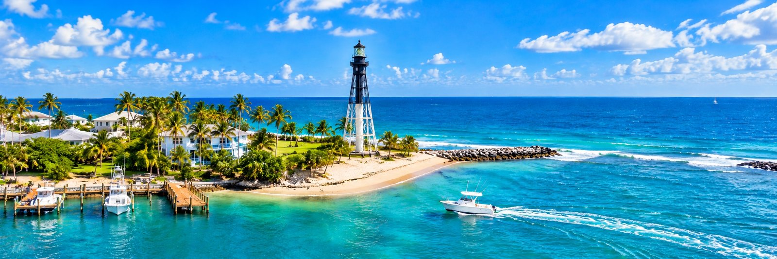 Panoramic view of Hillsboro Beach featuring the historic lighthouse, turquoise Atlantic waters, tropical palm trees, and boats near the inlet.