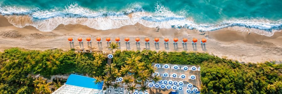 Aerial view of Jupiter Beach Resort & Spa with turquoise Atlantic water, sandy beach, umbrellas, and tropical landscaping.