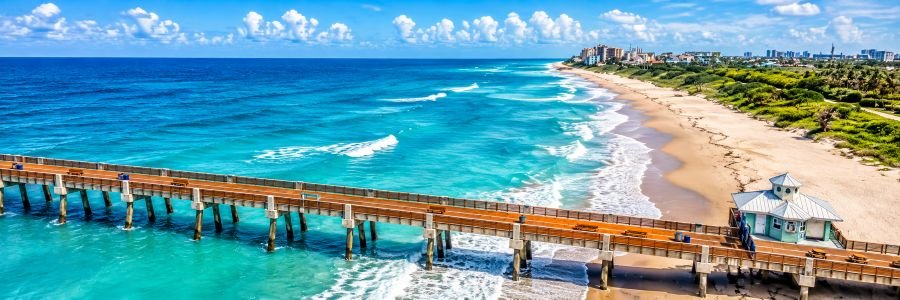 Aerial view of Jupiter Florida coastline with turquoise Atlantic water, sandy beach, and a long ocean pier.
