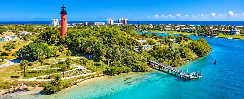Aerial view of the Jupiter Inlet Lighthouse surrounded by turquoise water, lush greenery, and the Jupiter Florida coastline.