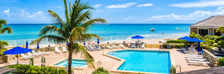 Jupiter Reef Club with a beachfront swimming pool, palm trees, blue umbrellas, and turquoise Atlantic Ocean views.
