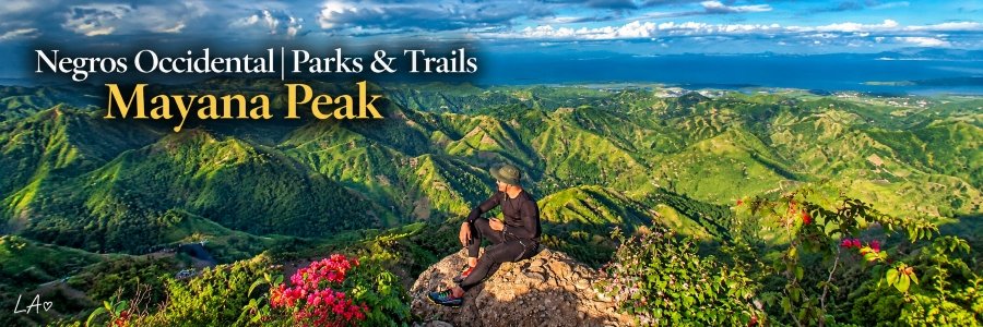 Hiker sitting on a rocky mountain overlook surrounded by rolling green hills, colorful wildflowers, and dramatic clouds beneath a blue sky.