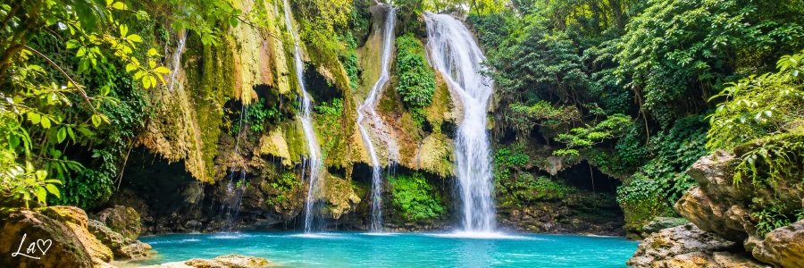 Tropical waterfall cascading over moss-covered limestone cliffs into a brilliant turquoise pool surrounded by lush rainforest.