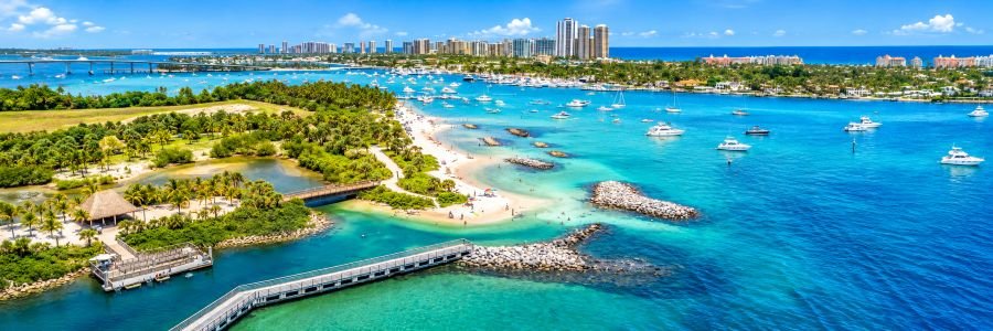 Aerial view of Peanut Island Park near Riviera Beach, Florida, featuring turquoise water, sandy beaches, tropical palm trees, and boats in Lake Worth Lagoon.