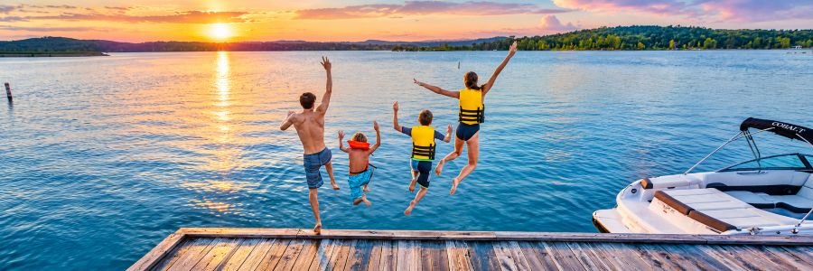 Family jumping from a dock into Table Rock Lake near Branson with a boat and forested Ozark hills