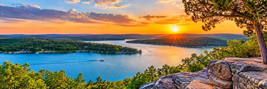 Table Rock Lake near Branson at sunset with blue water, forested Ozark hills, and a boat cruising across the lake